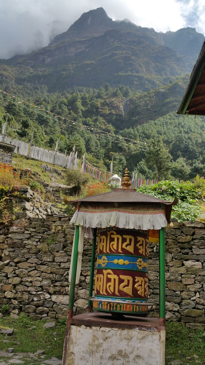 Eine buddhistische Gebetsmühle. Auf einem Schild wird auch der ungläubige Wanderer zum Drehen eingeladen, denn auch das erhöht nach buddhistischem Glauben das Wohl der Welt indem die auf den Mühlen aus sechs Wörtern bestehenden Mantras während des Drehens Licht zu allen fühlenden Wesen ausstrahlen und deren Leid beseitigen sowie schlechtes Karma auflösen.
